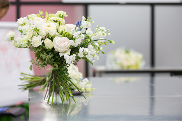 Beautiful bouquet of white flowers stands on the stems on a glossy gray table during the flower masterclass. Wedding decoration design concept