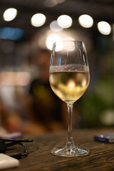 Glass of white wine in hand with blurred bokeh background. White wine glass outdoor shot.