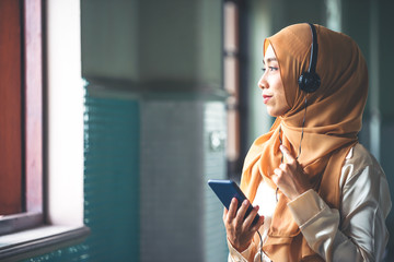 Portrait of a smiling young modern arabian woman holding mobile phone and listening the music to headphone.