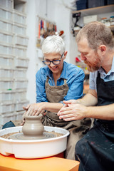 Senior woman spinning clay on a wheel with teacher at pottery class