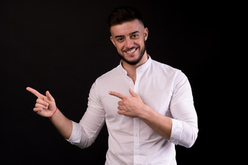 Casual young man pointing left to blank space, smiling. Copyspace, isolated on black.