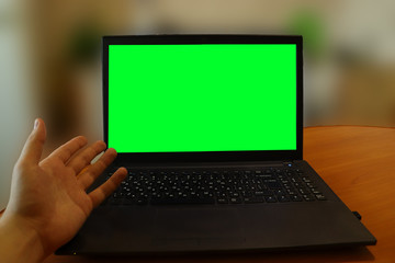 Laptop on a table with a green screen. A man has problems with a computer and shows the screen with...