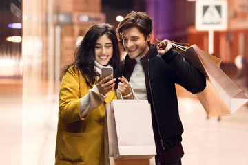 Consumerism concept. Couple with paper bags and smartphone