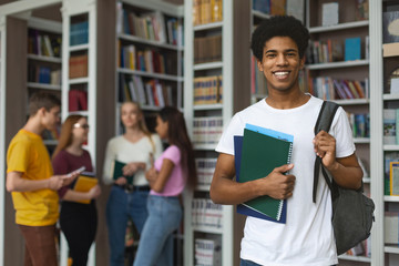 Excited african american student posing next to bookshelves in library