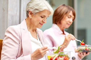 old age, leisure and food concept - senior women or friends eating takeaway salad on city street