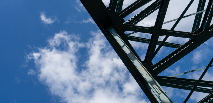 The Tyne Bridge in Newcastle, showing close up of the structure that makes up the top arch of the bridge against a blue cloud filled sky in summer.