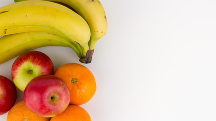 Overhead, closeup view of healthy fruit including Jazz apples, oranges and a bunch of ripe bananas featured on a white studio background.