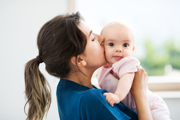 babyhood, motherhood and people concept - mother holding and kissing baby daughter at home