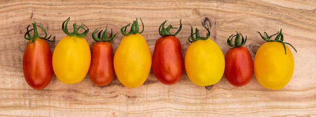 Fresh and ripe red and yellow cherry tomatoes on an old cutting board. Panoramic format