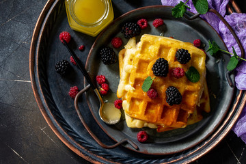 Breakfast. Homemade belgian waffles with berries and honey on dark table. Top view flat lay.