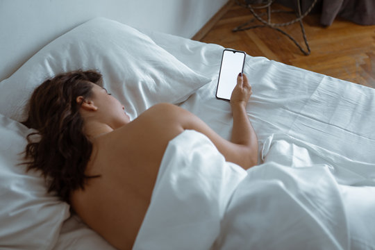 woman awake looking into smartphone white screen