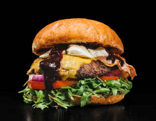 Craft burger is cooking on black background. Consist: sauce, arugula, tomato, onion, bacon, currant...