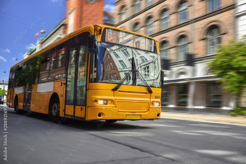 Wall mural yellow public bus speeding by city street