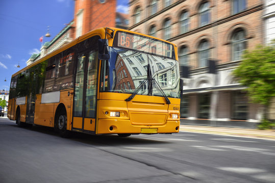yellow public bus speeding by city street
