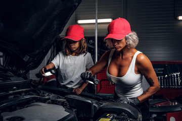 Professional mechanic woman and her little helper are making great team, working on car's engine.