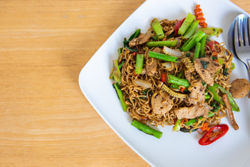 Spicy stir fried instant noodle and holy basil leaves on wooden table