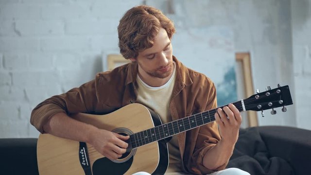 concentrated young man playing acoustic guitar on couch
