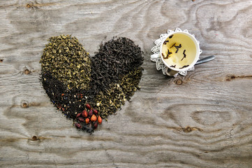 I love tea concept. Tea heart of different tea : green, black, floral over wooden background with tea cup