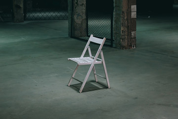 An empty chair in a dark room. A lonely object standing in empty concrete walls at dusk, a...