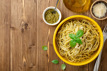 Spaghetti pasta with sauce pesto and parmesan cheese in ceramic bowl on wooden table