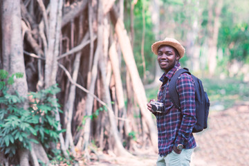 Naklejka na ściany i meble Portrait of African man traveler explorer with photo camera in forest.
