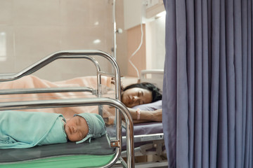 Obraz na płótnie Canvas Asian newborn baby laying in crib with his mother lying on bed side in the hospital