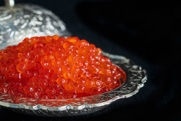 Red caviar in silver bowl on black background
