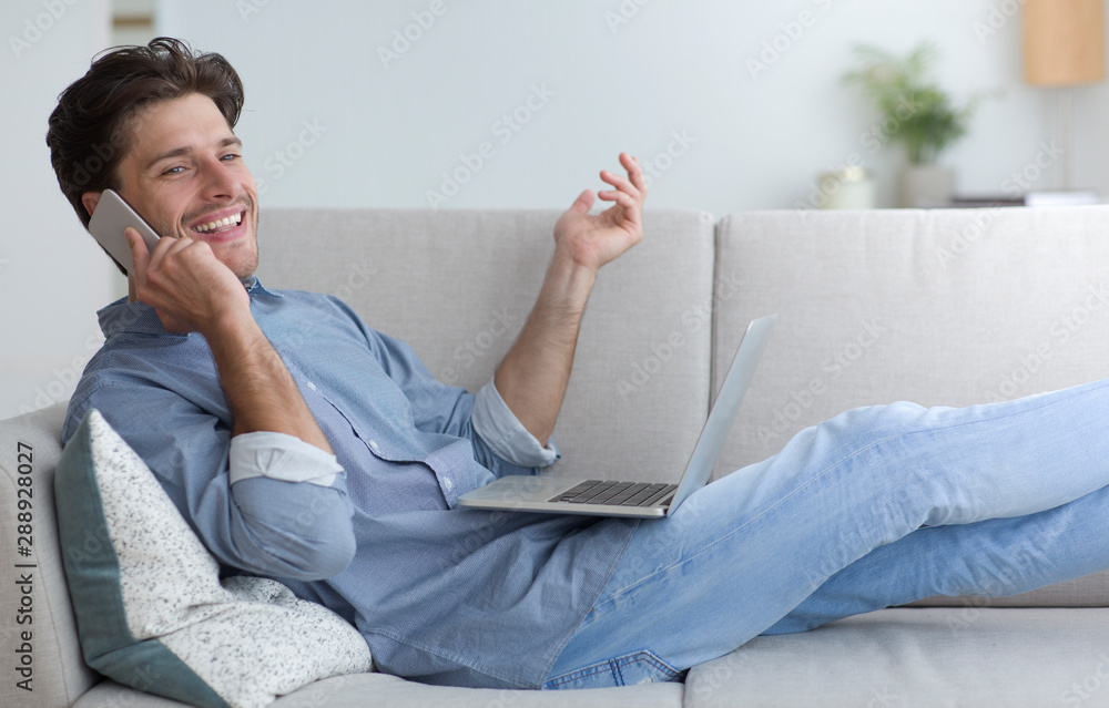 Poster man talking on phone working on laptop lying on sofa