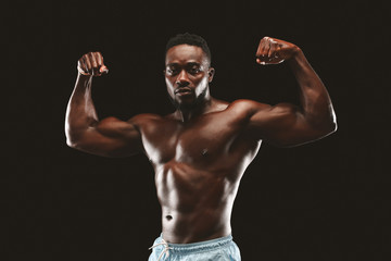 Fototapeta na wymiar Athletic african guy flexing muscles over black studio background
