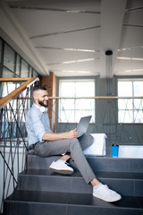 Bearded man holding his silver laptop and working hard