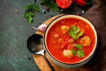 Tomato soup with meatballs and chili peppers on a dark stone or slate table. Free space for your text.