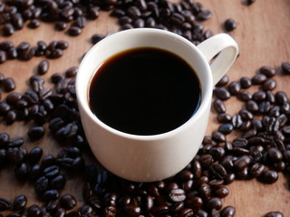 cup of coffee with beans on wooden background
