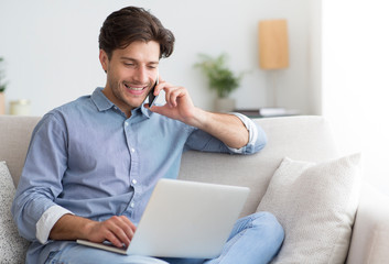 Young entrepreneur talking on cellphone working at laptop at home
