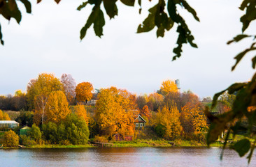 Beautiful autumn landscape with wooden private houses and agricultural buildings on riverbank, colorful autumn trees and blue sky. Outdoor recreation and countryside life concept. Autumn scene.
