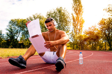 Muscular sporty fitness man checking training schedule and workout plan in a park