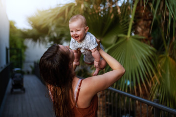 Happy Caucasian mom holding her cheerful son in the air while standing outdoors.