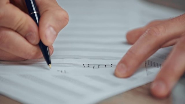 partial view of musician writing notes on music sheet