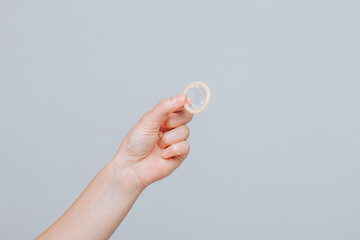 Female hand holding condom close up on grey background