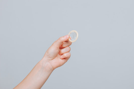 Female hand holding condom close up on grey background