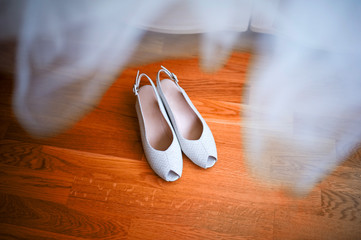shoes of the bride stand on a wooden floor, top view. Bridesmaid dress hanging over the shoes