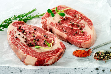 Two raw marbled beef steak ribeye with spices on white Kraft paper. The concept of organic fresh meat