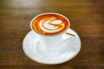 cappuccino coffee cup with beautiful latte art on old dark wooden table in coffee shop.