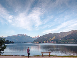 Beautiful scene at park. Man is standing adove bench and bicycle lane, mountain lake in the Alps, Zell am See, Salzburger Land, Austria, view from Wiesenlehen. travel tourism concept design