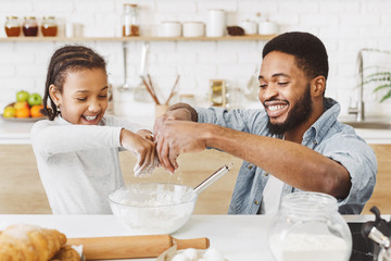 Cheerful daddy and daughter adding flour into dough bowl
