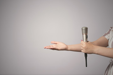 Wireless microphone in female hand isolated on gray background.