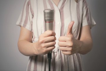 Woman with a wireless microphone in hands on a gray background. Good speech concept.