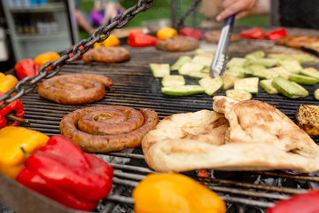 A large round grill on the coals in which grilled color vegetables and fresh meat sausages are cooked. Food and equipment for cooking at a food festival