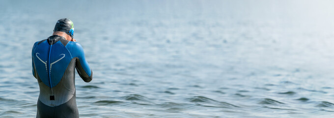 Panorama of a triathlete in a wetsuit getting ready to swim right before a triathlon 