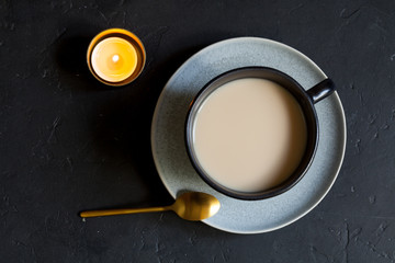 Cup of hot cocoa and candle on black background, flat lay