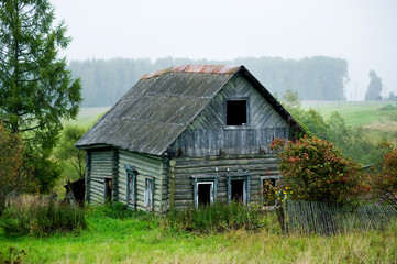 old abandoned rickety old wooden house without windows with a partially missing fence.